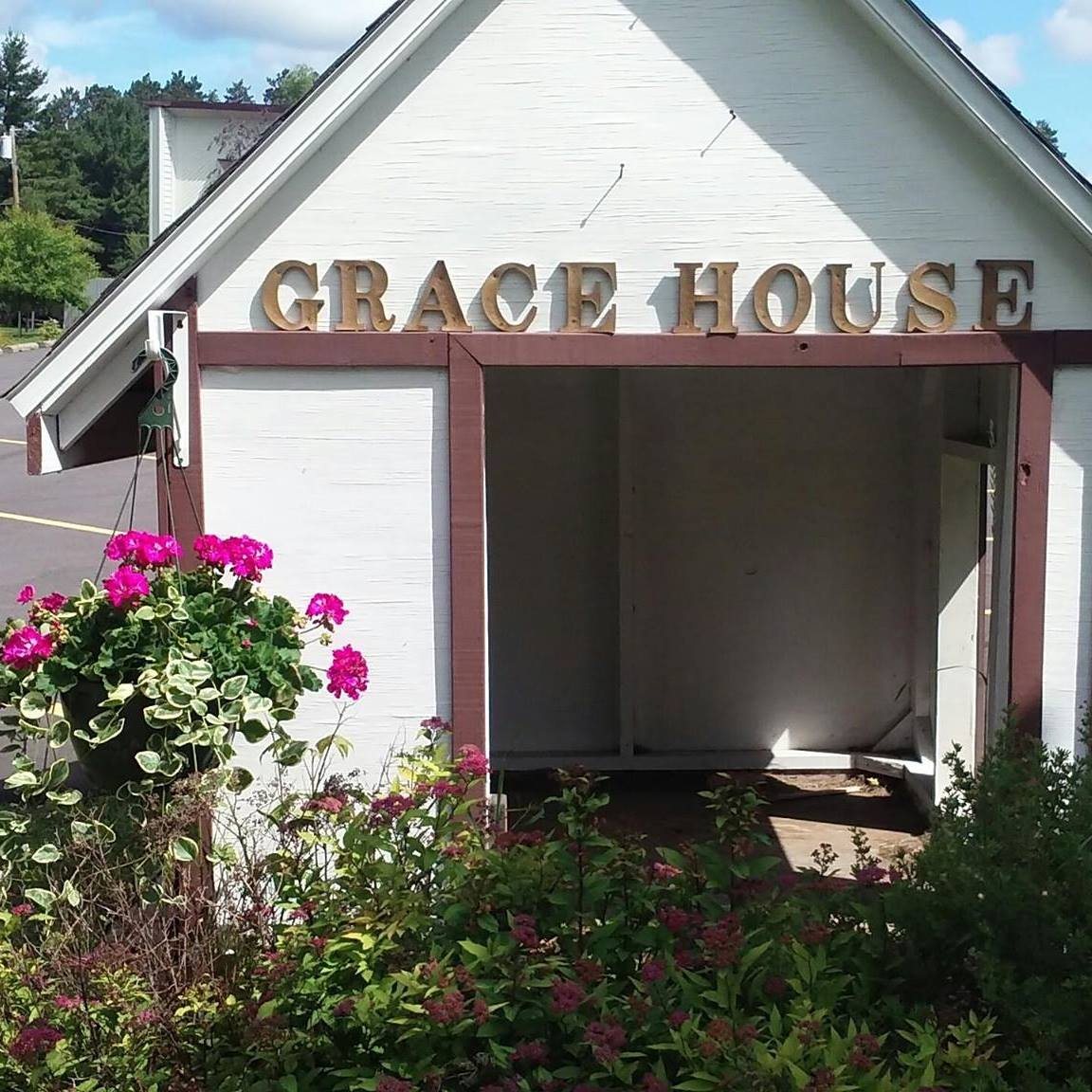 The Grace House entrance — a white gabled porch with GRACE HOUSE spelled in wooden letters above the door, flower baskets blooming beside it